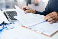 Foto: Person mit Dokumenten und Laptop