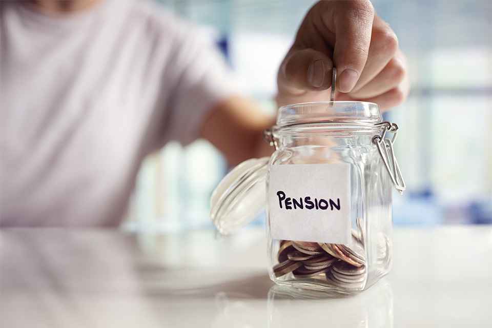 Foto: Person wirft Münzen in Glas mit Aufschrift Pension